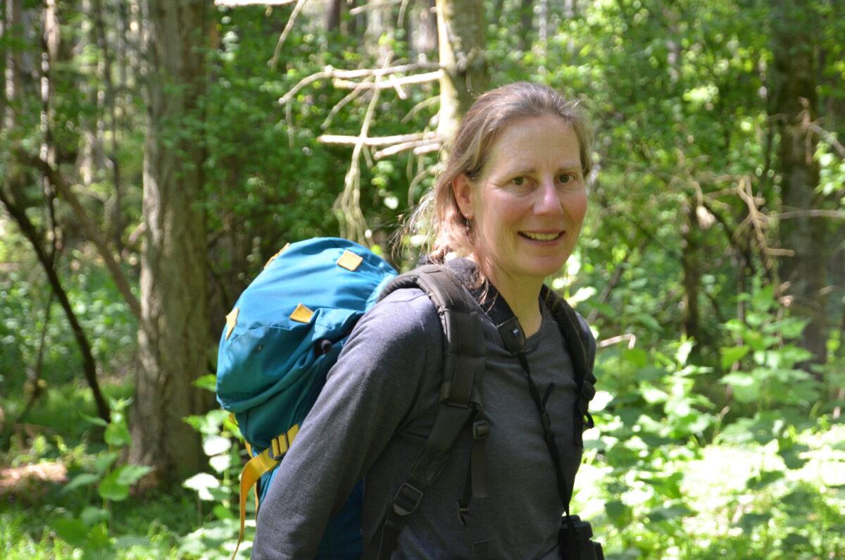 A woman with a blue backpack on in the forest.