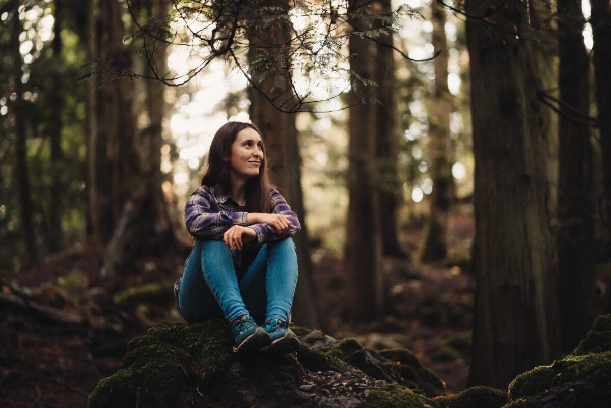 A girl in jeans sitting in the forest.