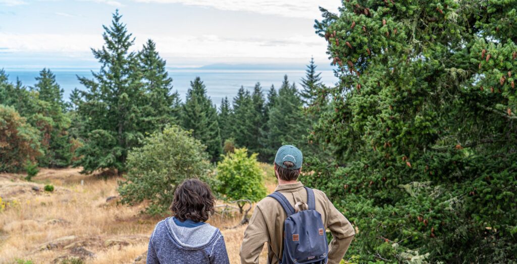 Two hikers overlooking a sunny water view from the hilltop of the future Mt Ben West Preserve on the Westside of San Juan Island